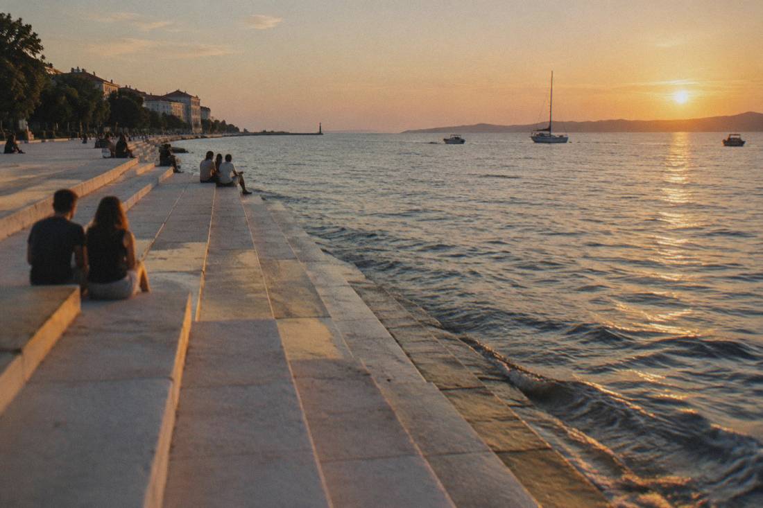 Wide pale stone steps going down into the calm Adriatic on the Zadar seafront at golden hour, a few people sitting at a distance