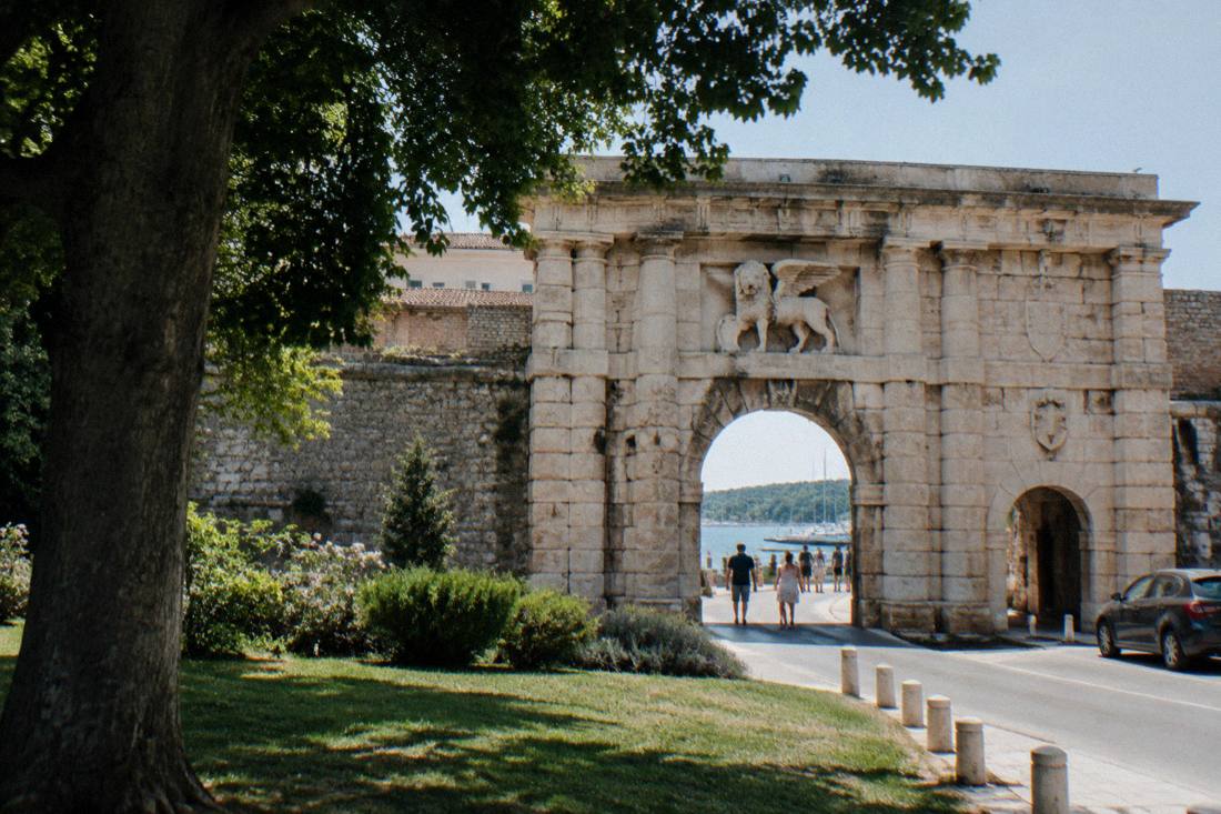 A grand Renaissance stone gateway with a wide central arch and a smaller side arch in the Zadar city wall at midday