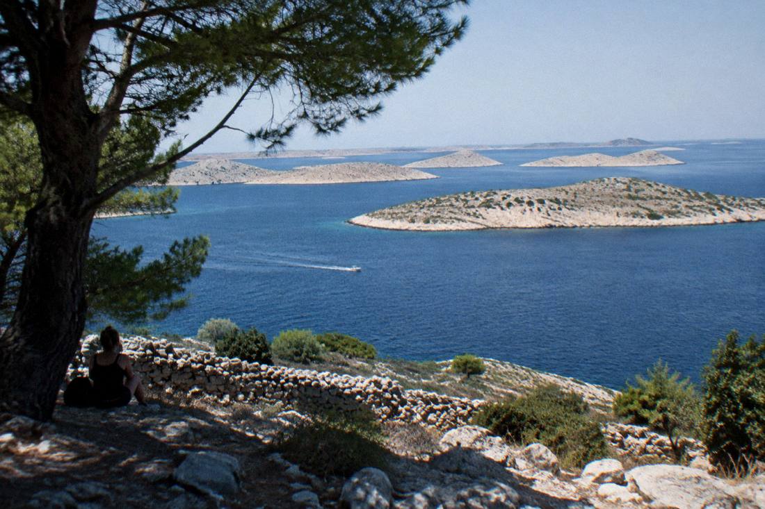 Bare white limestone islands scattered across deep blue sea in the Kornati, a small boat leaving a thin wake