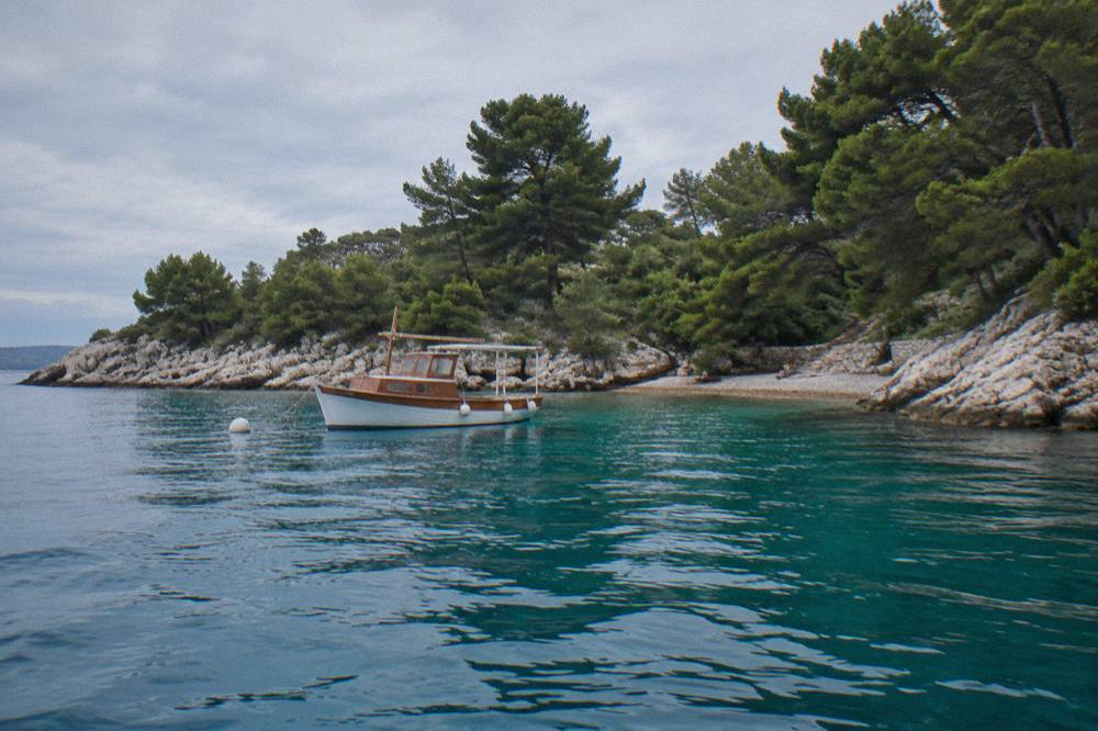 A boat anchored in a clear blue cove with rocky pine-covered shores near Ugljan island