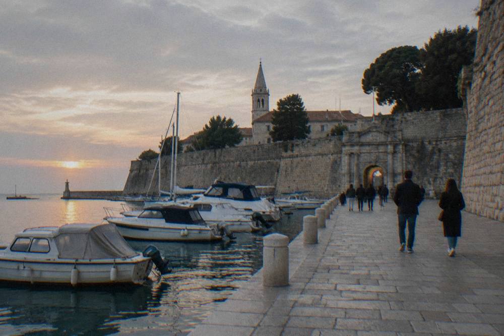 Walkers on the stone waterfront promenade beside Zadar's old town walls at golden hour