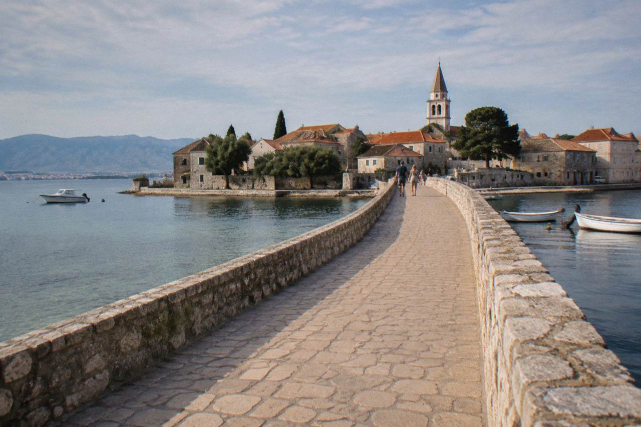 A small stone bridge over shallow lagoon water leading to the old town of Nin