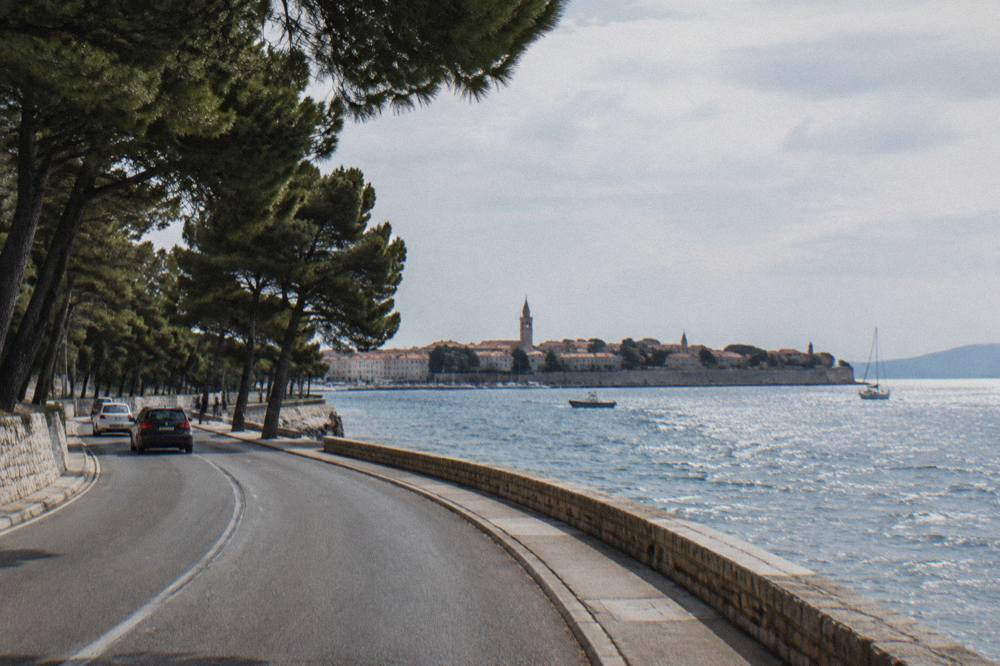 A pine-lined coastal road curving beside the sea toward Zadar's peninsula