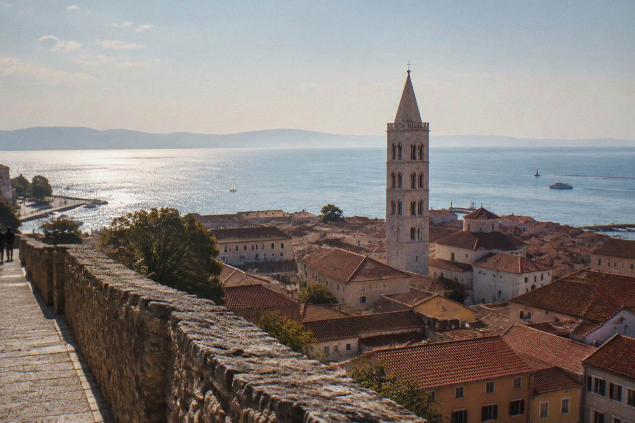 Terracotta rooftops and a bell tower of Zadar Old Town with the Adriatic glittering behind, from a high wall
