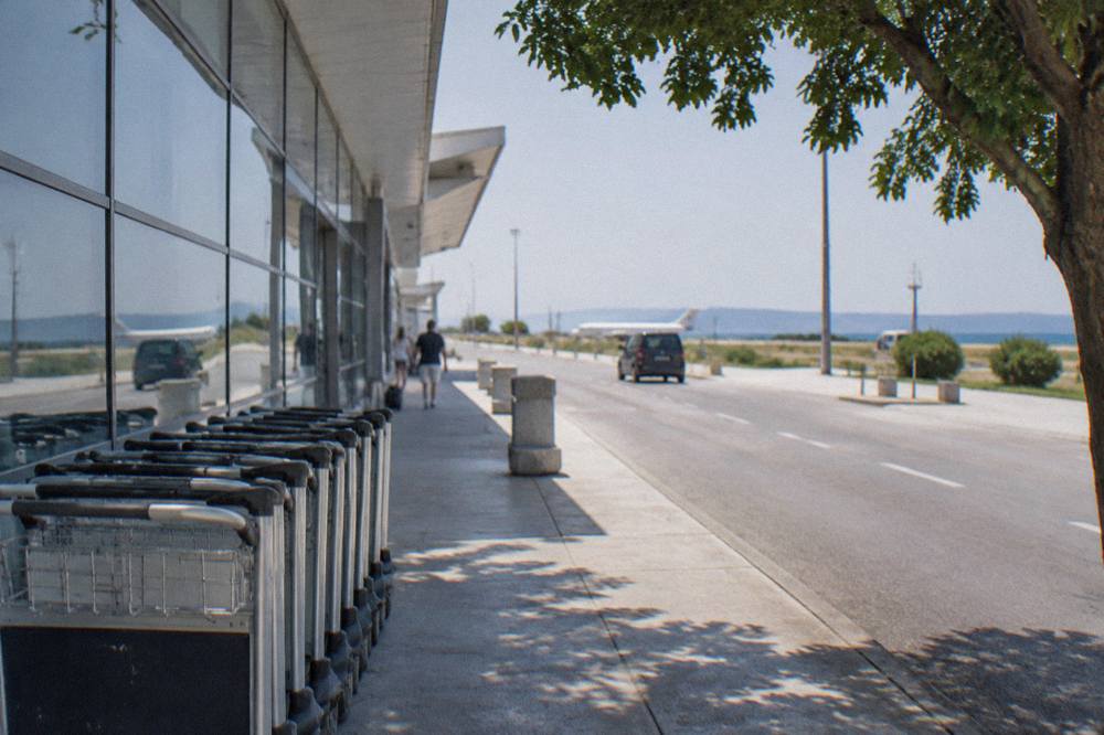Empty luggage trolleys lined up along a quiet kerbside outside a small airport terminal