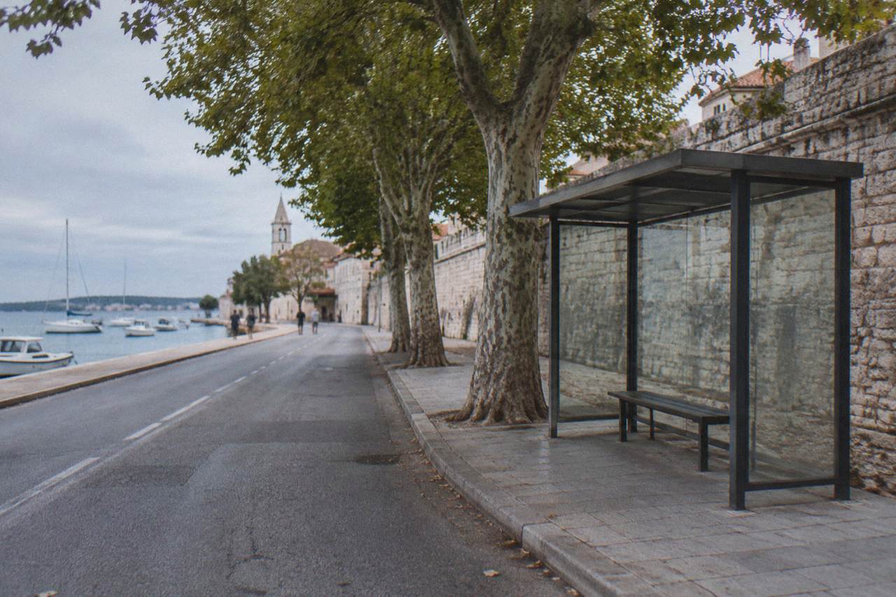 A plain bus stop shelter beside a stone wall at the edge of Zadar Old Town in the shade
