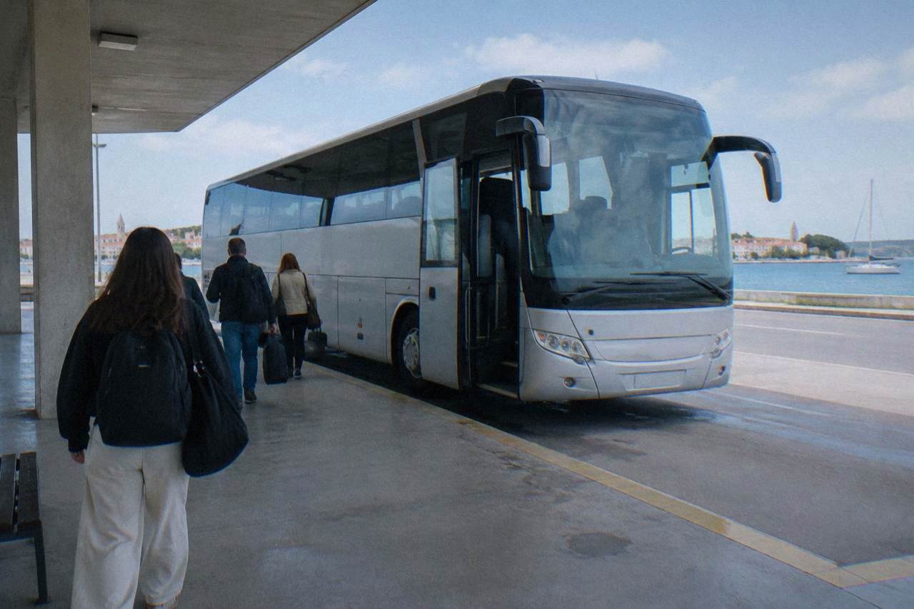 A long-distance coach with open doors at a bay of Zadar bus station, passengers seen from behind