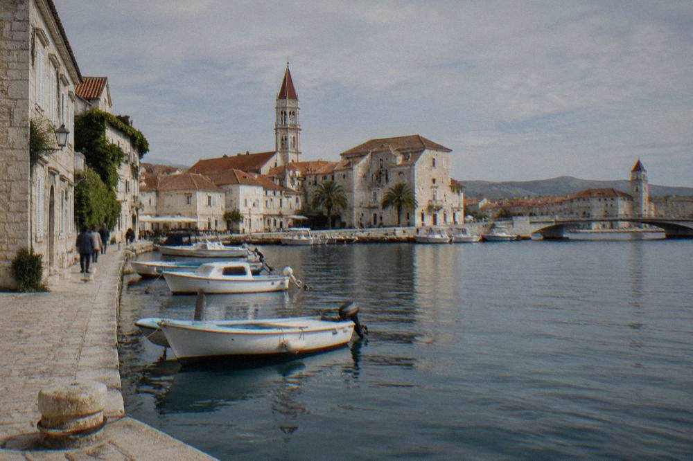 Trogir's pale limestone harbour front with terracotta roofs and moored boats in midday light