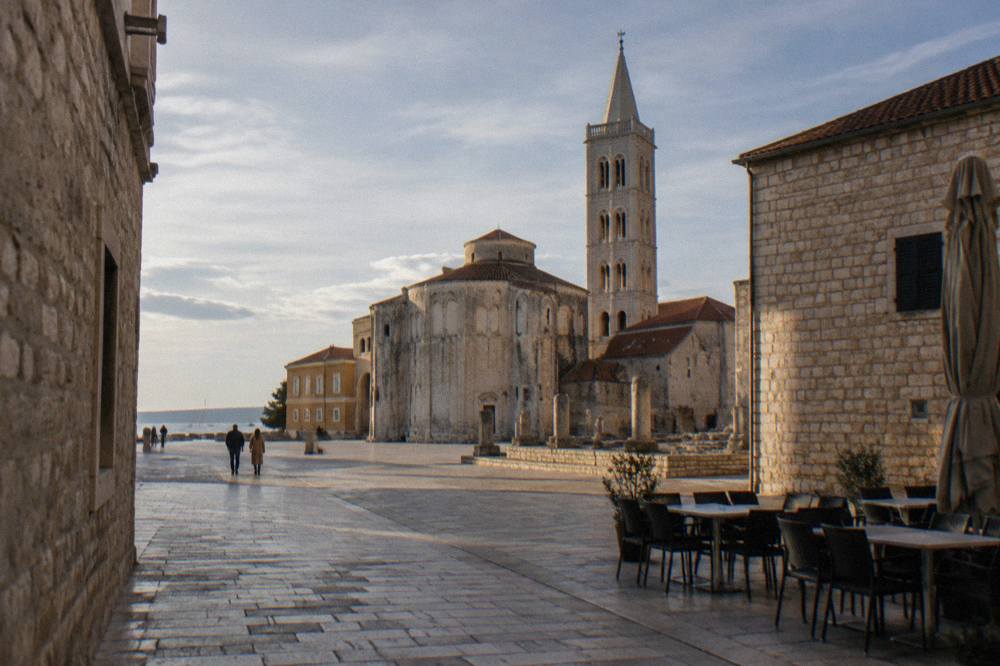 Quiet old town square in Zadar in late afternoon light with warm stone walls and empty cafe chairs