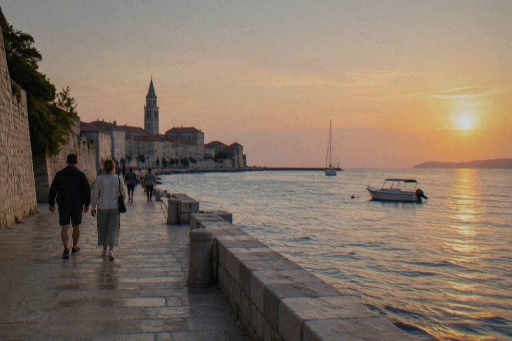 People walking the stone waterfront path beside Zadar's old town at golden hour