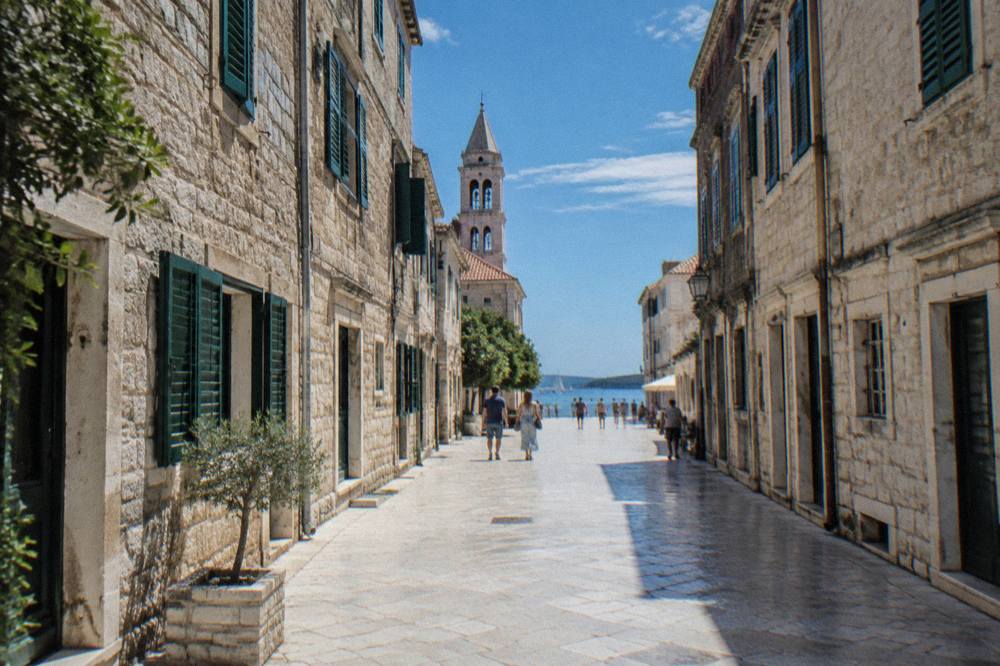 Sunlit white limestone lane in Zadar Old Town with stone facades and green shutters