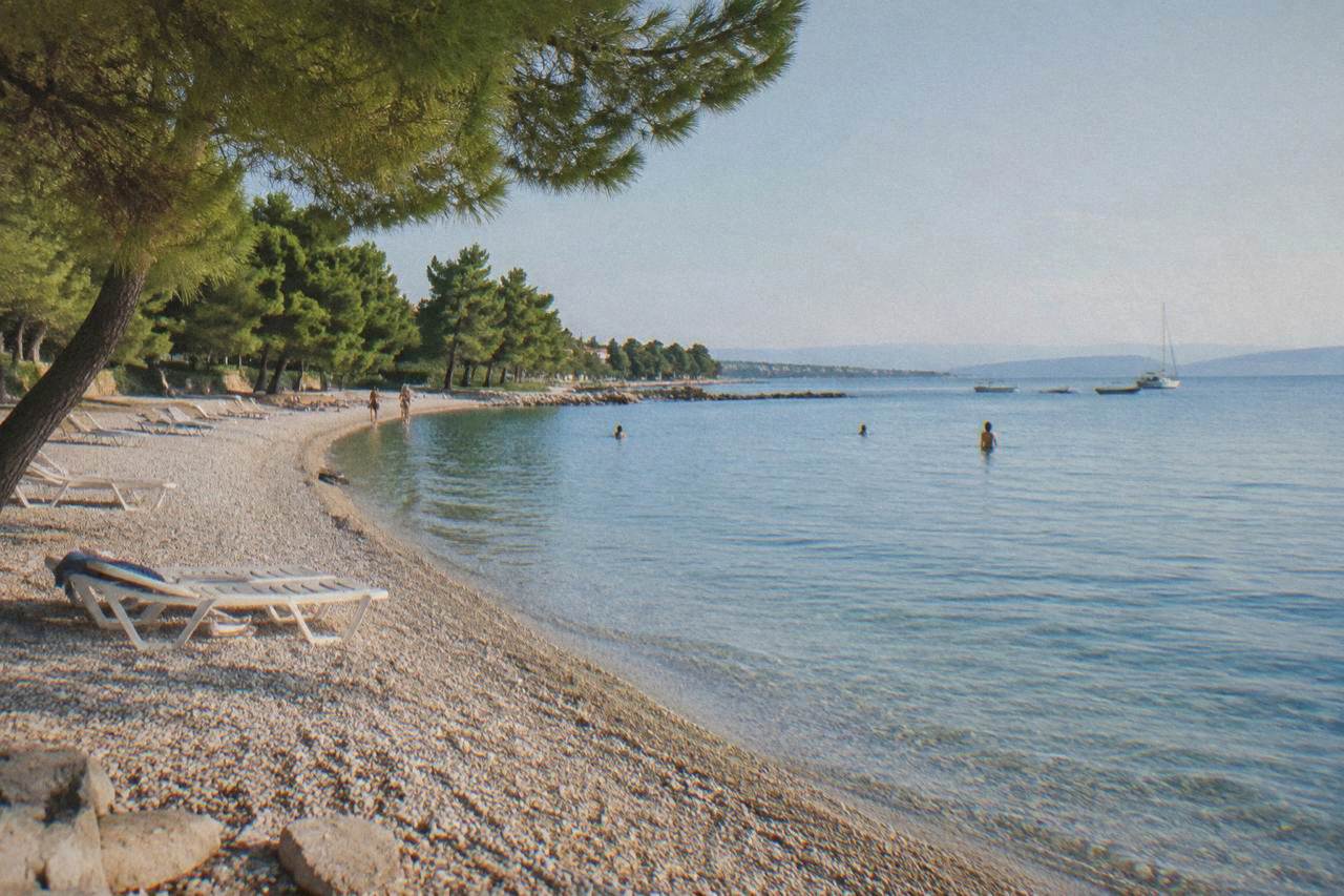 Curving pebble beach in Borik backed by low pines with calm blue shallow water