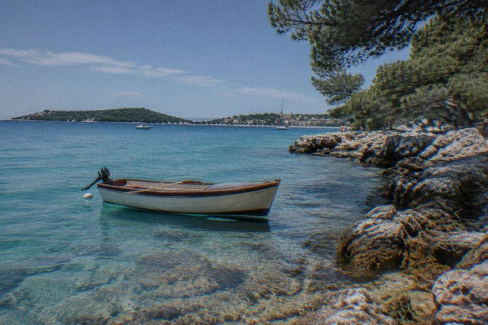 Wooden boat anchored in a turquoise cove with rocky shore and pines on Ugljan island