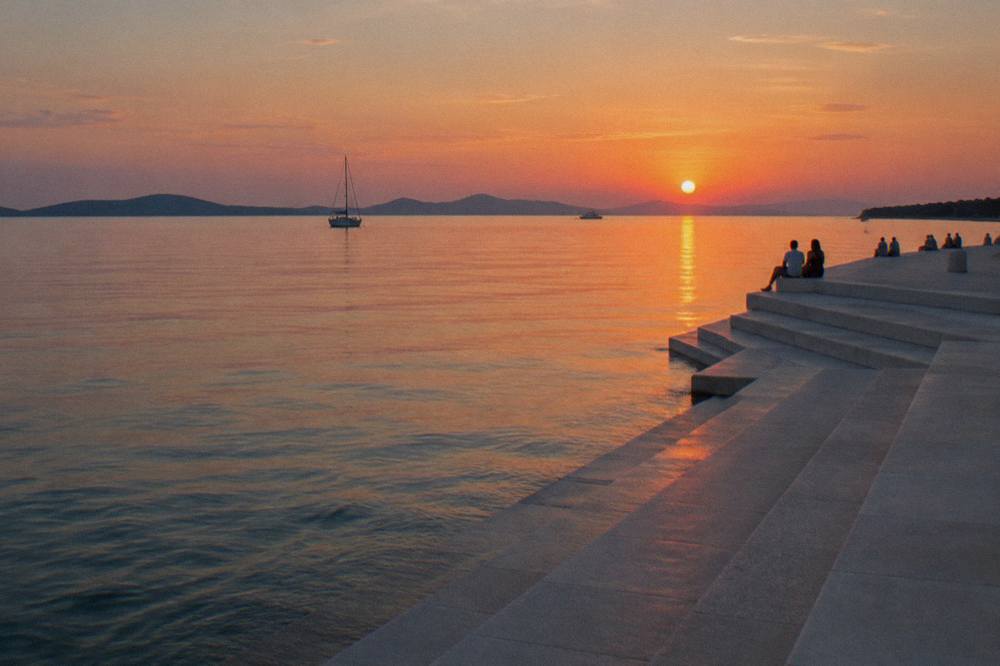 Wide stone steps of the Sea Organ meeting the sea at sunset with islands on the horizon