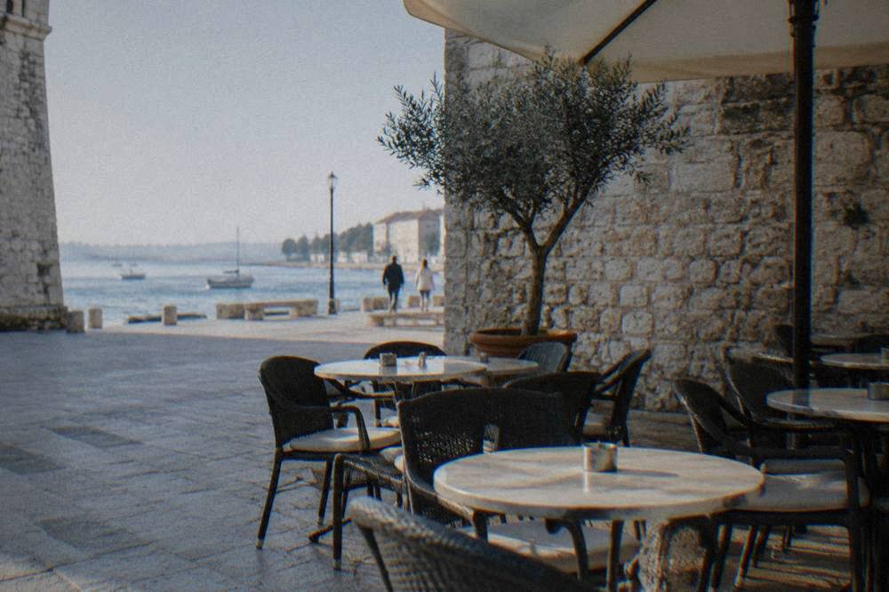 Empty cafe terrace in shade near Five Wells Square with old stone walls behind