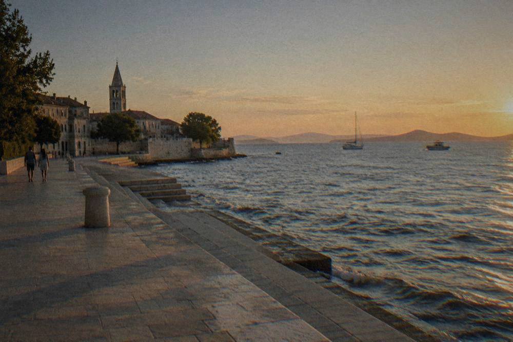 Zadar seafront promenade at golden hour with stone steps to the water and distant islands