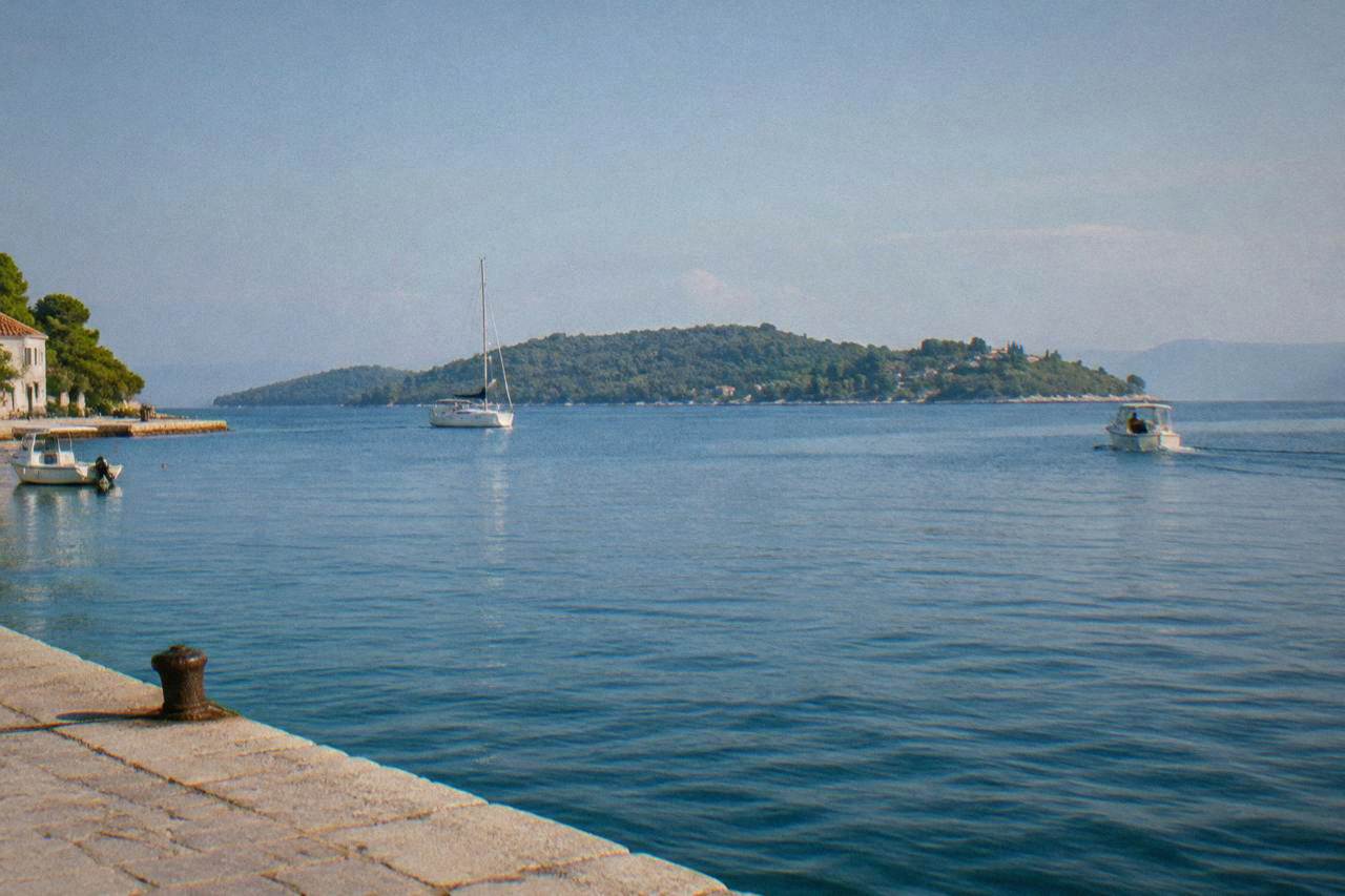 View across calm blue water toward green Ugljan island from a stone quay near Zadar