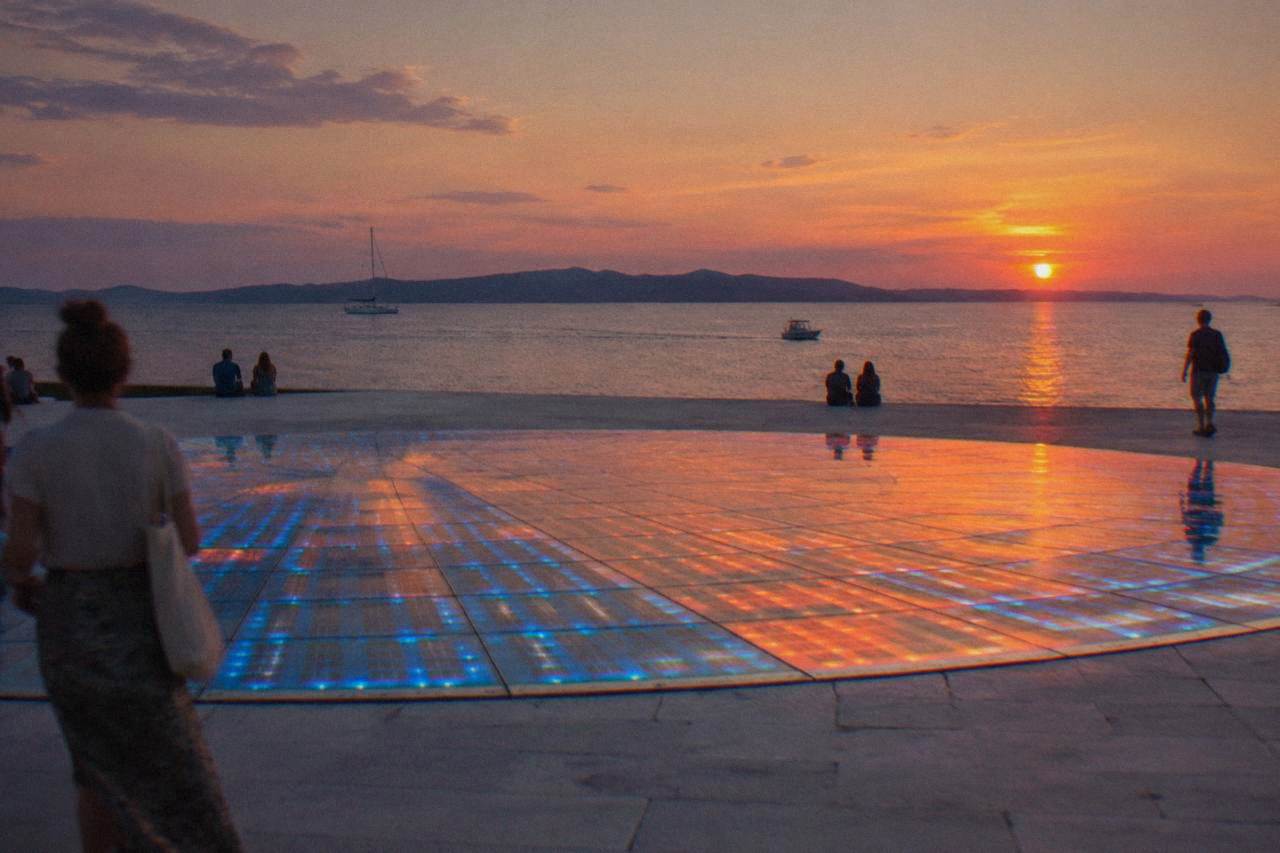 Circular glass installation glowing blue and orange on the Zadar waterfront at dusk