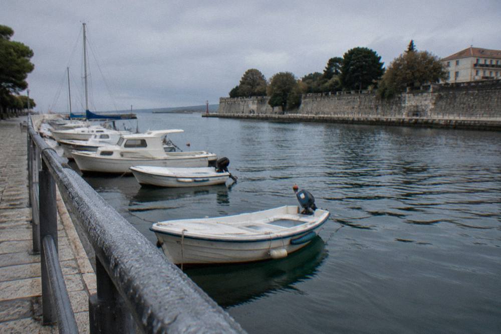 Raindrops on a harbour railing with moored small boats under a grey sky in Zadar