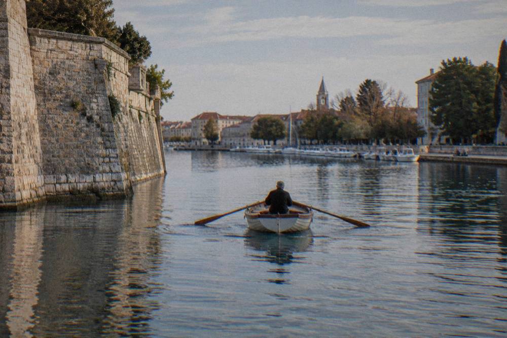 Small wooden rowing boat crossing Zadar's old harbour beside the stone city wall