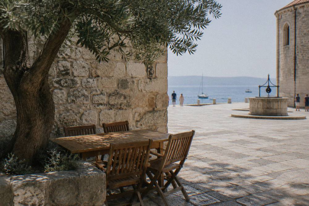 Shaded old town corner in Zadar with an empty wooden table, olive tree and stone wall