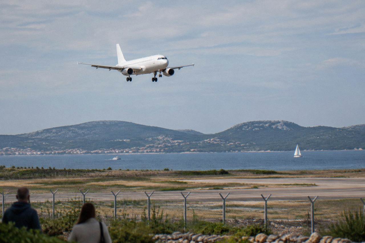 A white passenger aircraft descending over karst hills and the Adriatic coast near Zadar