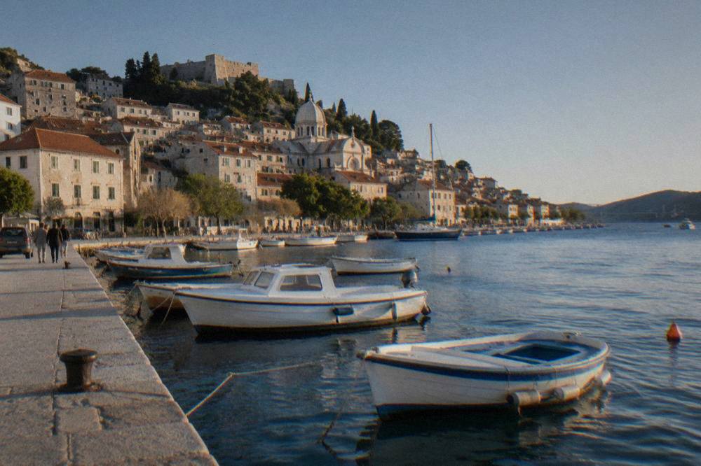 Small boats moored beside a stone quay in Šibenik with old stone houses on the hillside
