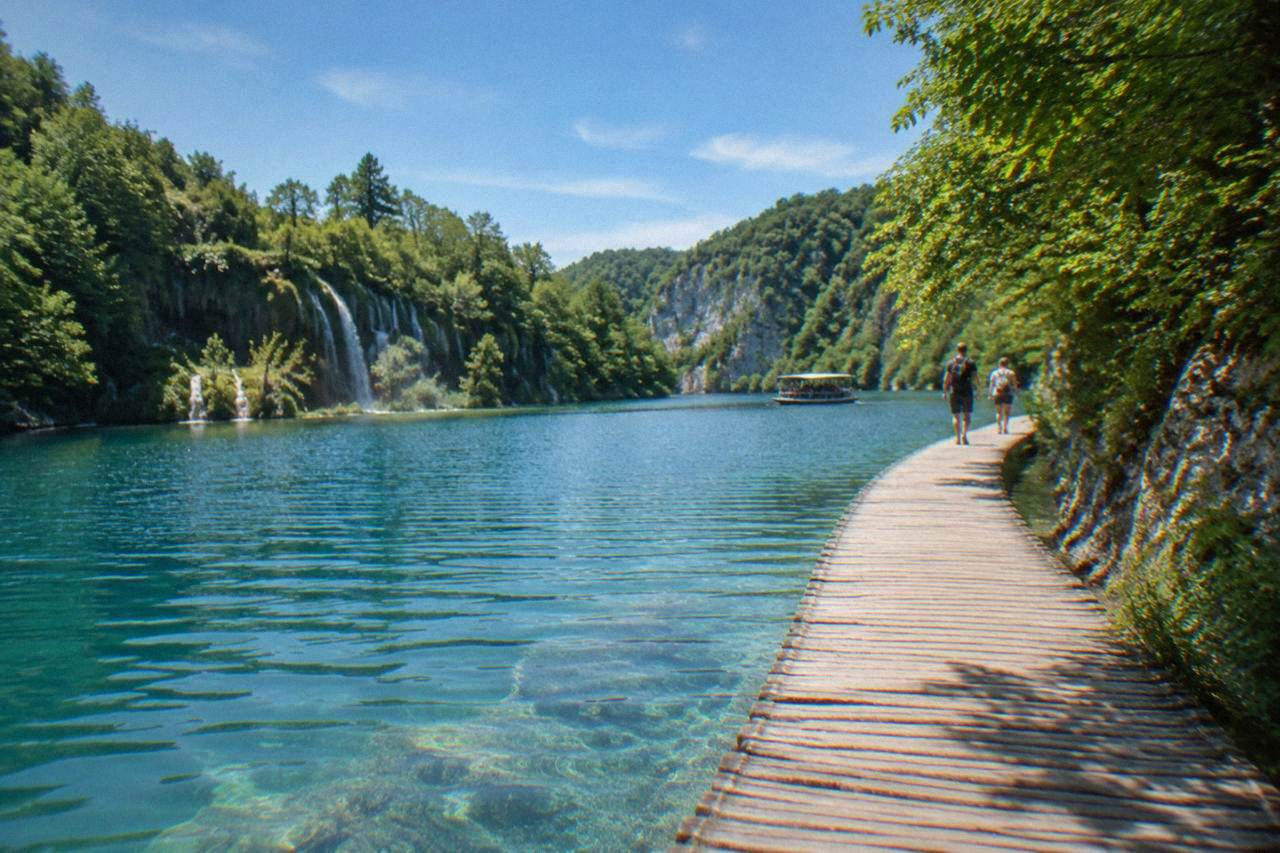 Wooden boardwalk crossing turquoise lake water at Plitvice Lakes in summer light