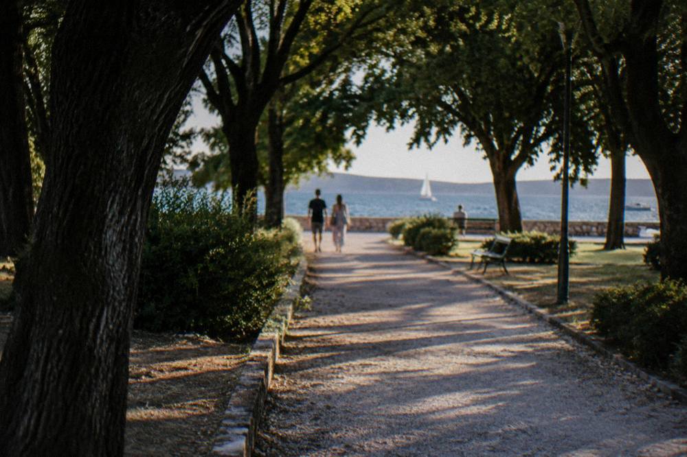 Shaded gravel path in a Zadar park leading under trees toward the sea