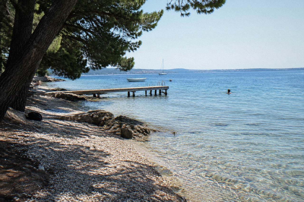 Small stony beach at Diklo with a wooden jetty and pines