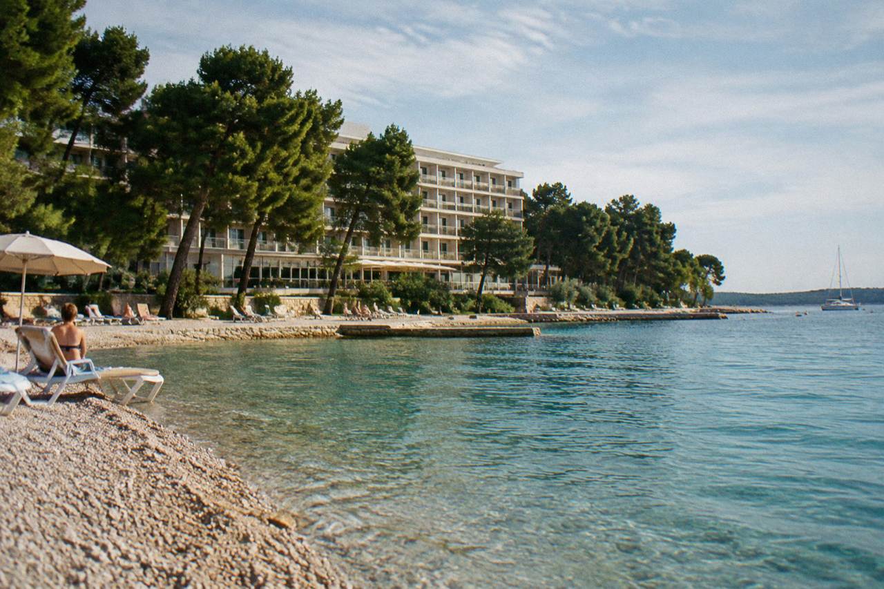 Hotel behind the pebble beach at Kolovare with pines and calm sea
