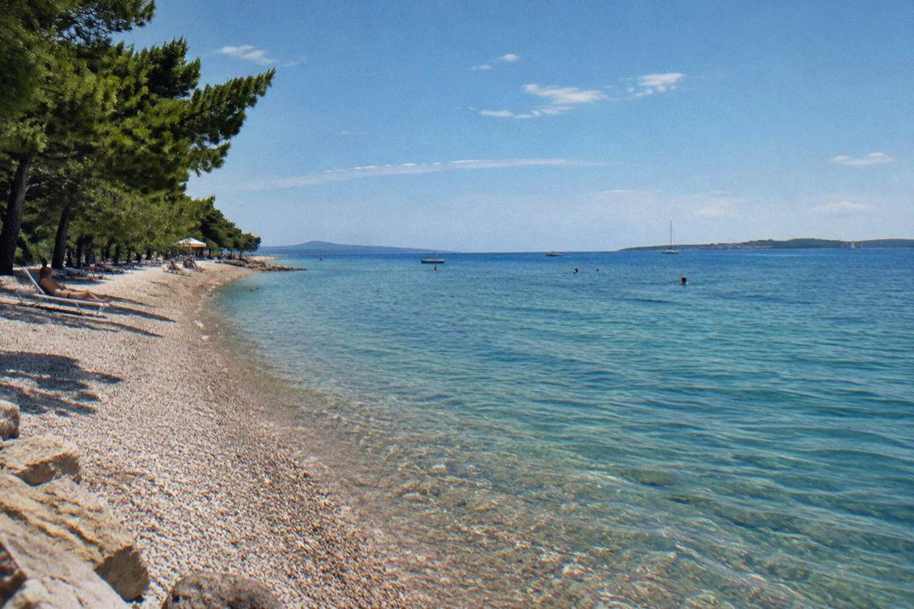 Pebble beach at Puntamika with clear water and pines behind