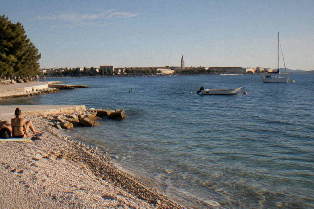 Puntamika pebbles and turquoise water with the Zadar waterfront across the bay