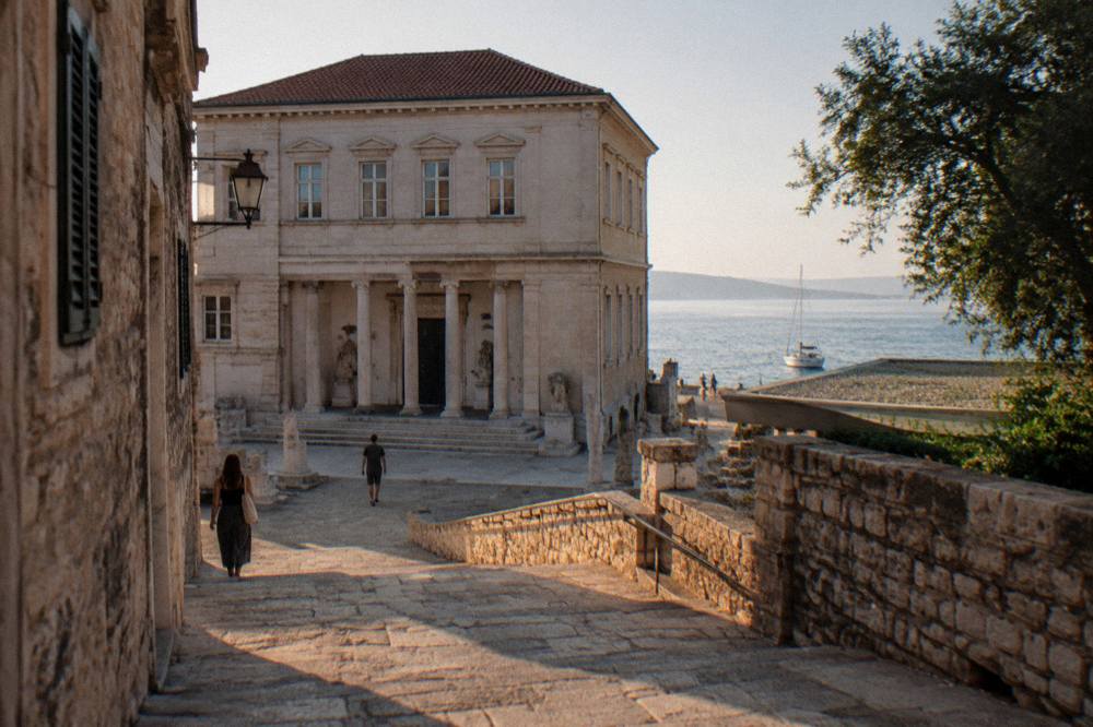 Stone steps from a sunny Old Town lane toward the museum facade