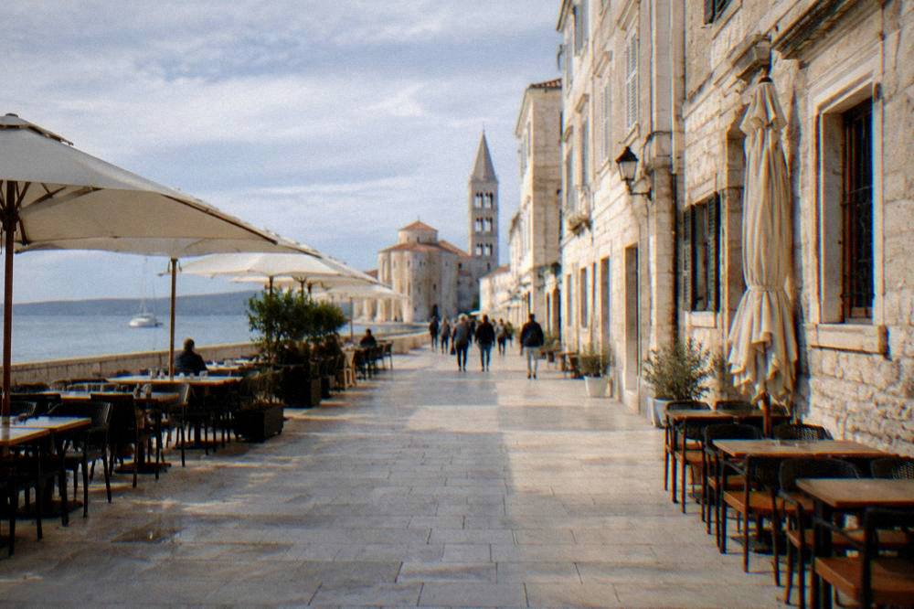 Stone-paved Old Town main street with cafe tables at midday