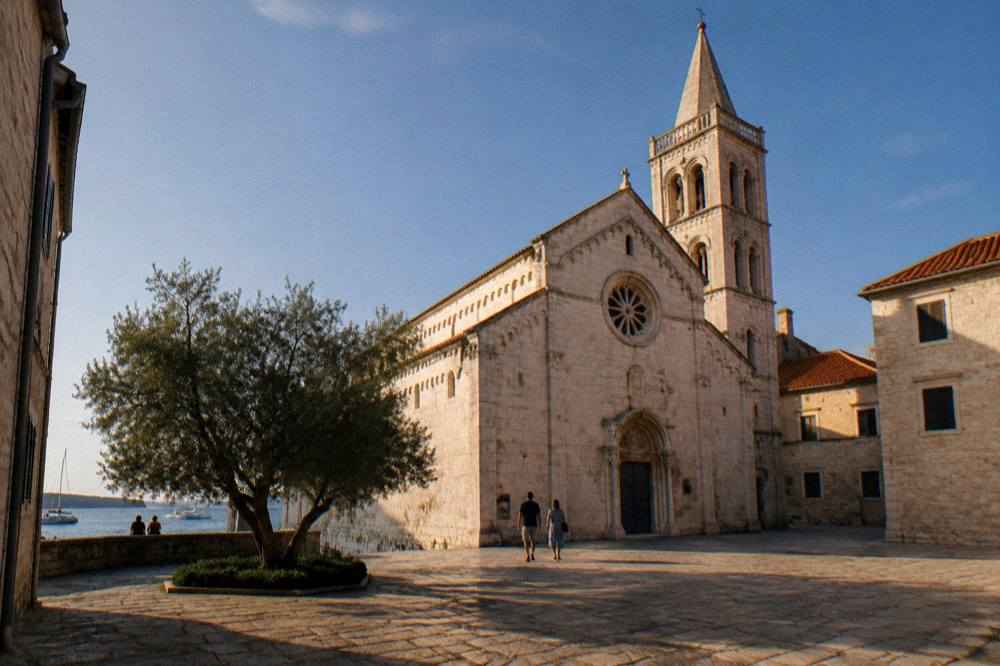 Cathedral seen across a side square with terracotta roofs on a clear day