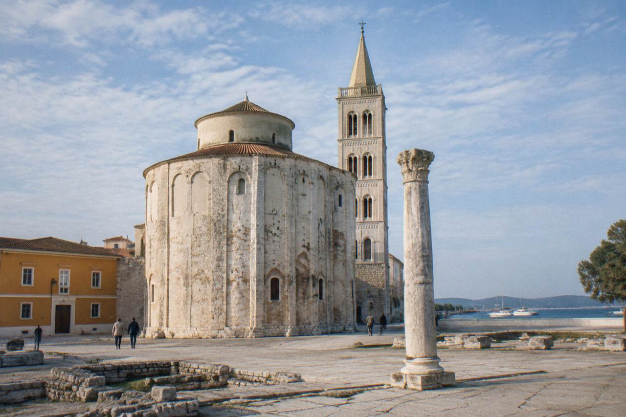Round pale stone church beside a Roman column in the square