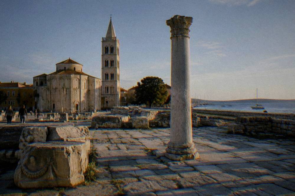 Roman column and ancient paving beside a bell tower on a clear day