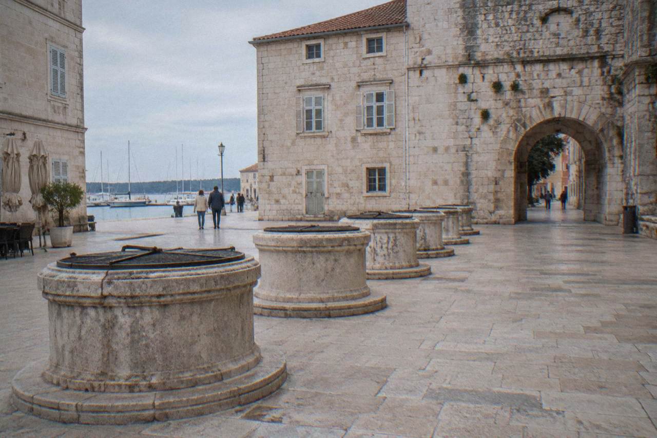 Five circular stone well-heads in a small paved square in soft natural light