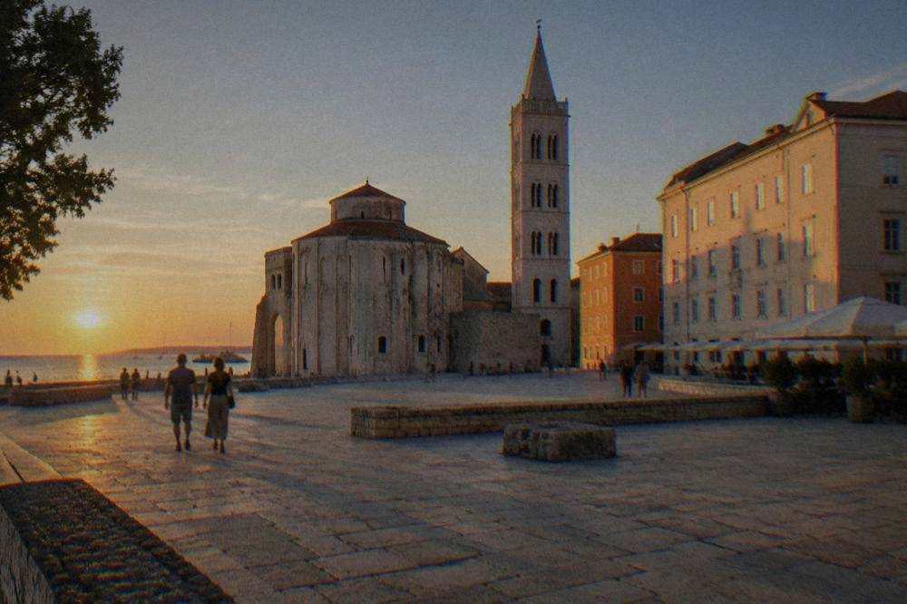 Old paved square with pale buildings and a slender tower