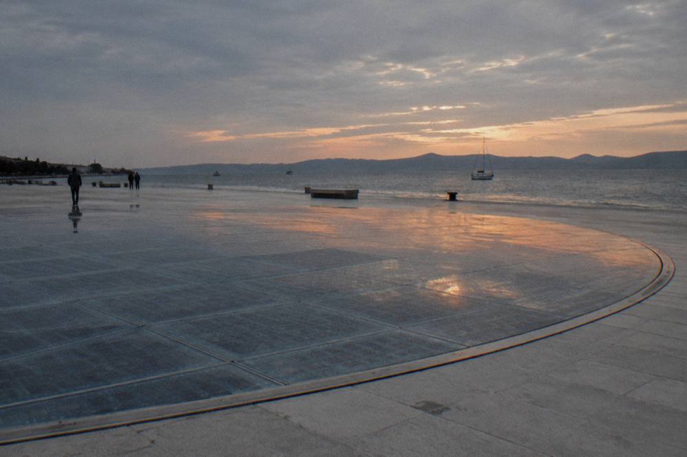 Circular glass-panel installation reflecting an orange sky in summer light