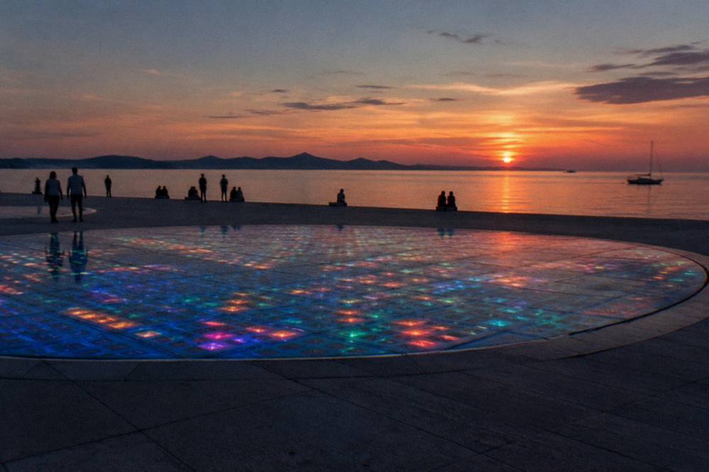Glass circle glowing at dusk with distant silhouettes and calm sea