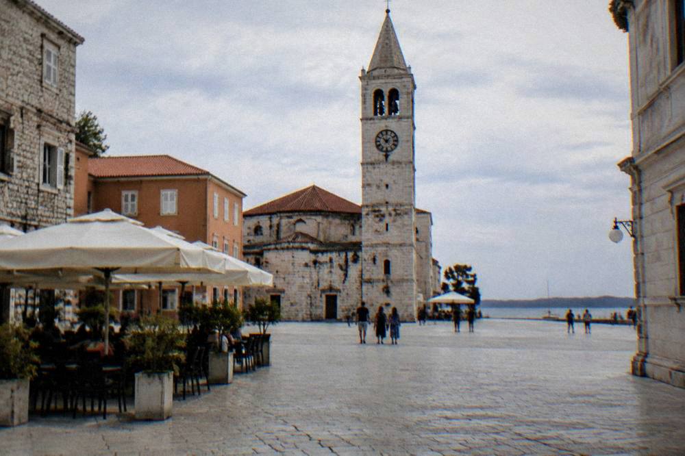 Open stone square with a clock tower and cafe parasols
