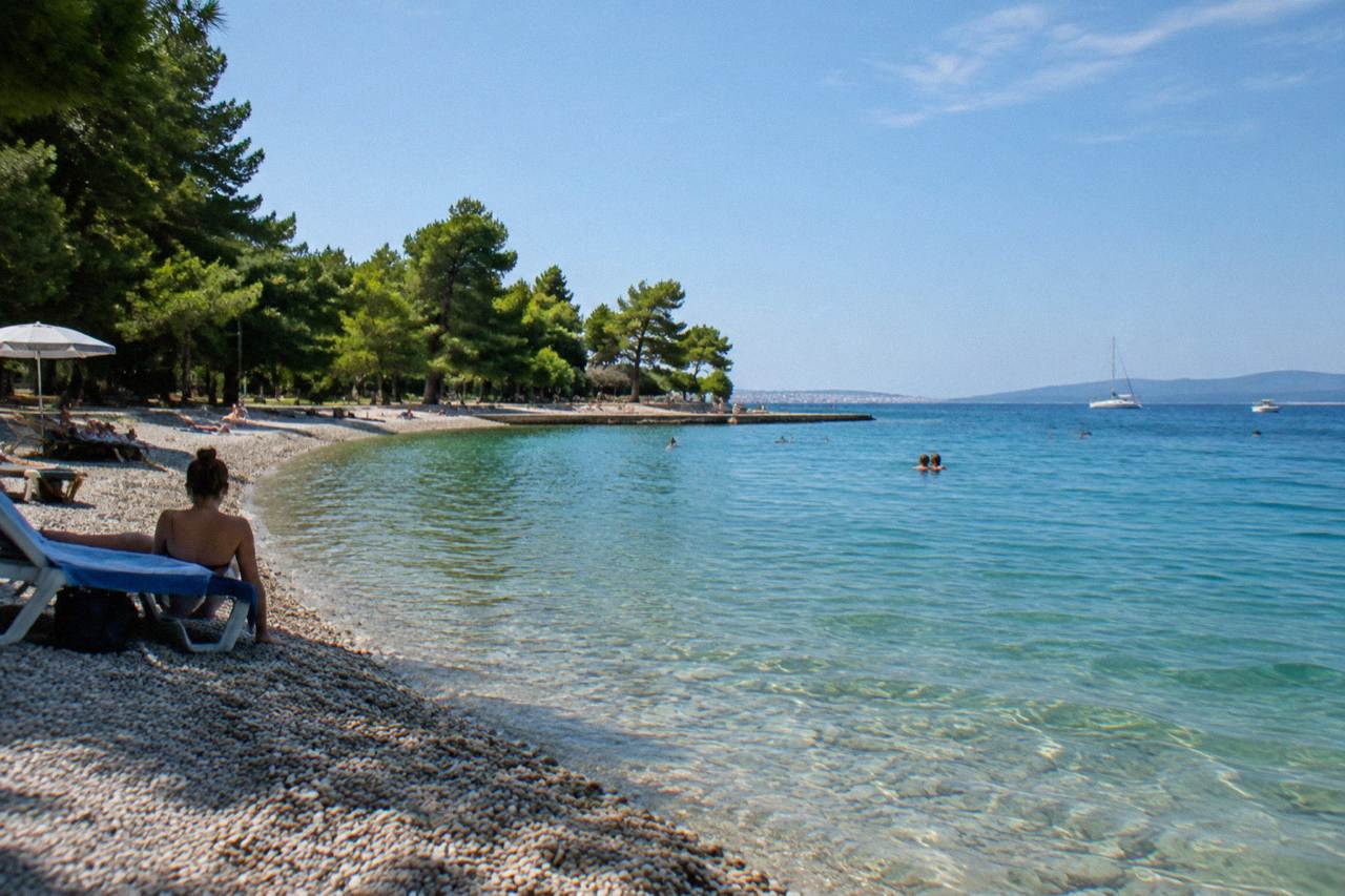 Crescent pebble beach at Kolovare with turquoise water and pines