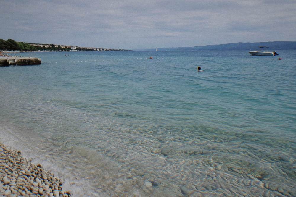 Clear shallow water over pale pebbles with a distant swimmer