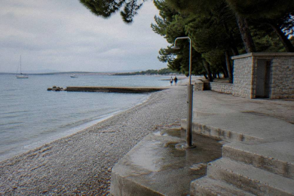 Stone steps and beach shower under pine shade at Kolovare