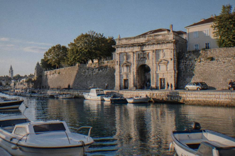 Stone gate seen across a small harbour basin with moored boats