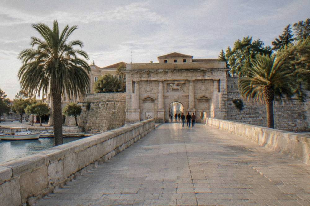 Distant pedestrians crossing a stone bridge toward the gate arch