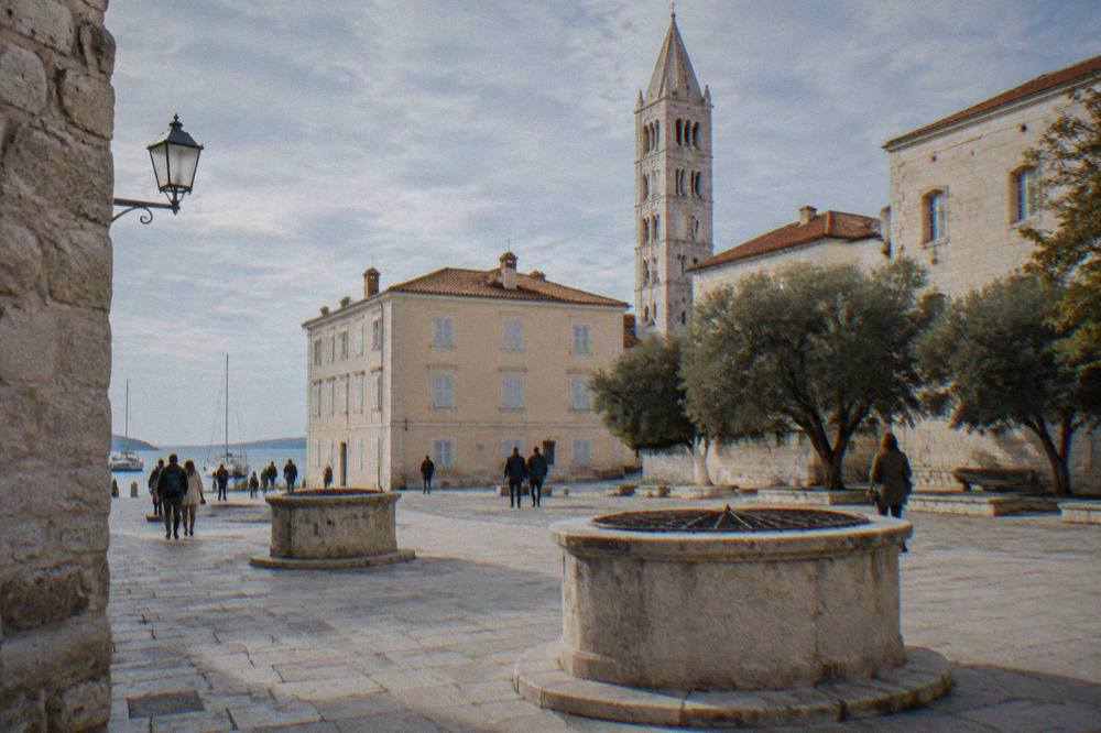 Small paved square with circular well-heads and a slender tower
