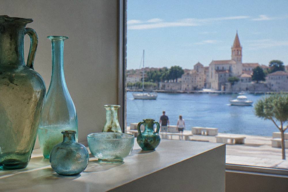 Ancient blue-green glass vessels on a plain pale shelf in soft natural light